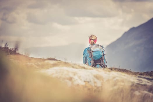Woman in sportswear and with backpack is sitting on the stony ground and enjoys the view, in the mountains