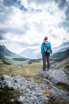 Woman in sportswear and with backpack enjoys the view in the mountains
