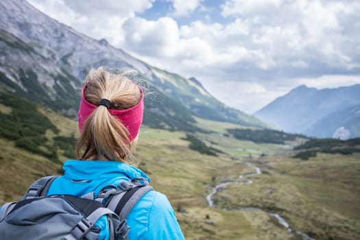 Woman in sportswear and with backpack enjoys the view in the mountains