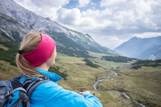 Woman in sportswear and with backpack enjoys the view in the mountains