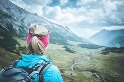 Woman in sportswear and with backpack enjoys the view in the mountains