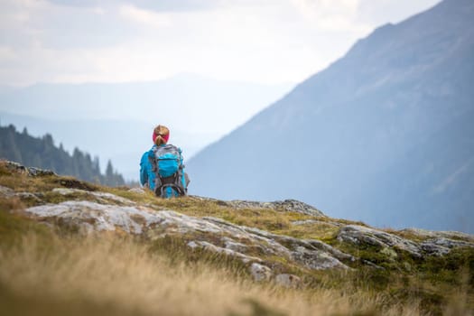 Woman in sportswear and with backpack is sitting on the stony ground and enjoys the view, in the mountains