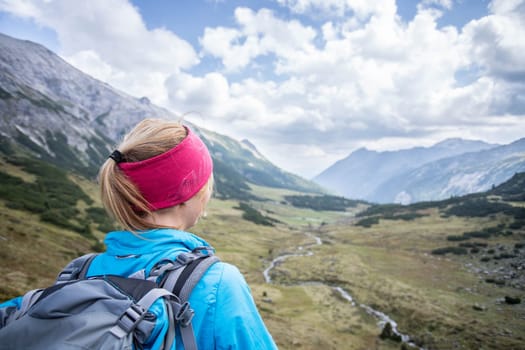 Woman in sportswear and with backpack enjoys the view in the mountains