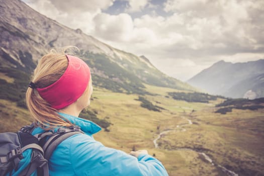 Woman in sportswear and with backpack enjoys the view in the mountains