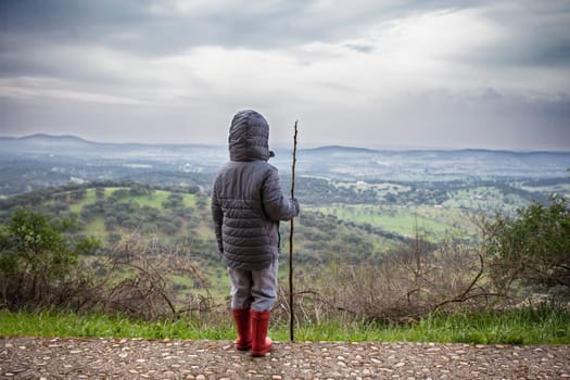 Child boy observing the dehesa landscape outskirts Alburquerque, Extremadura, Spain. He holds a cane over cloudy sky