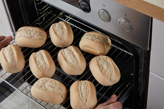 From above anonymous person placing glide rack with bread buns in fan oven
