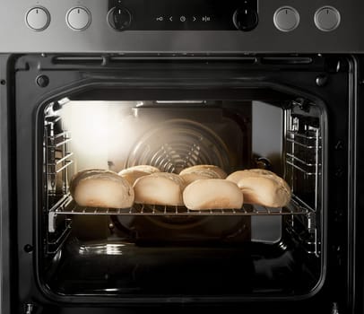 Rack of baking raw buns inside of modern oven appliance with lamp burning