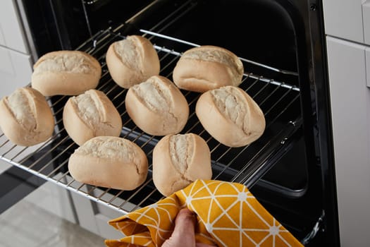 From above faceless person with towel removing hot glide rack with fresh bread buns out of oven