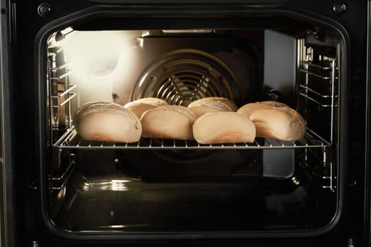 Metal rack with half baked bread buns loaded in modern fan oven for baking
