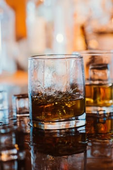 whiskey glass with ice and warm light on black table with reflection, warm atmosphere