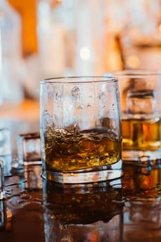 whiskey glass with ice and warm light on black table with reflection, warm atmosphere