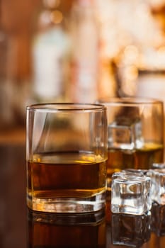 whiskey glass with ice and warm light on black table with reflection, warm atmosphere