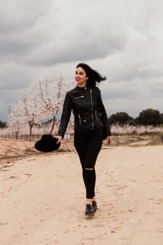 Brunette woman with leather jacket walking on a path with flowered almond trees