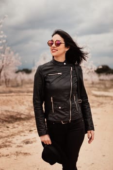 Brunette woman with leather jacket walking on a path with flowered almond trees