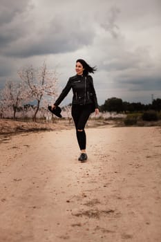 Brunette woman with leather jacket walking on a path with flowered almond trees