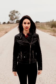 Brunette woman with black leather jacket in a lonely road