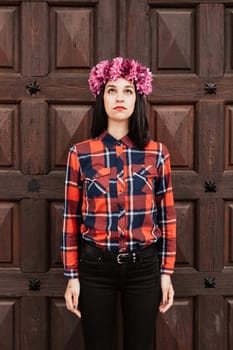 Pretty stylish girl with pink flower crown and red plaid shirt In front of a wooden door