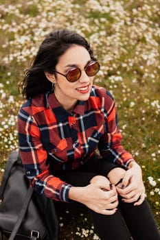 Beautiful woman with sunglasses sitting in the middle of a flowery meadow