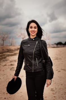 Brunette woman with leather jacket walking on a path with flowered almond trees
