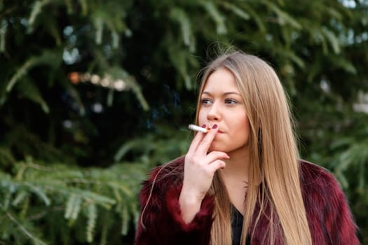 Pretty blond girl with long hair smoking in the park