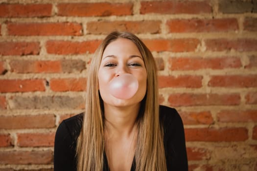 Funny girl making a pomp with a bubble gum and a brick wall of background