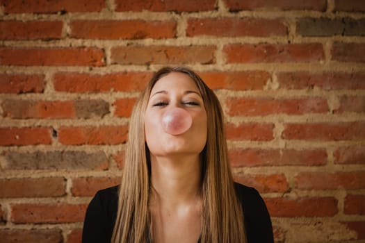 Funny girl making a pomp with a bubble gum and a brick wall of background