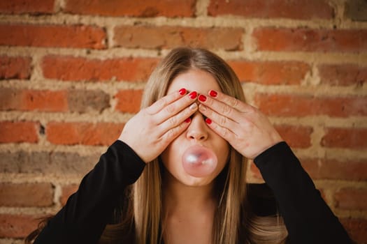 Funny girl making a pomp with a bubble gum and a brick wall of background