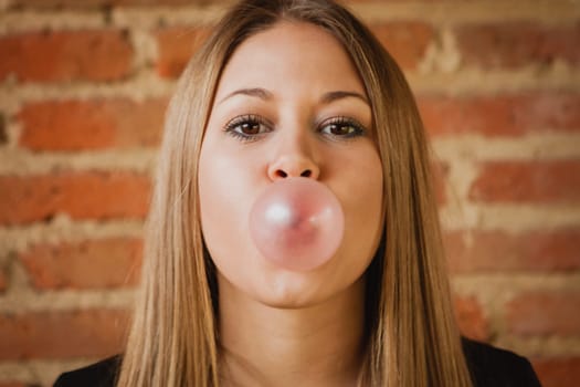 Funny girl making a pomp with a bubble gum and a brick wall of background