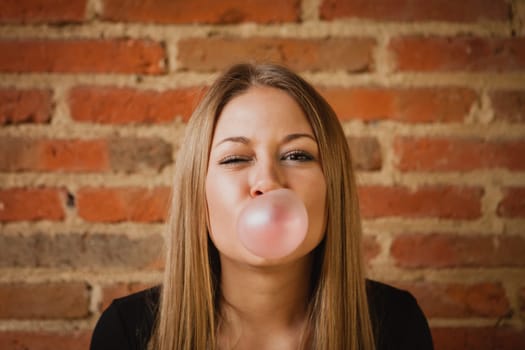 Funny girl making a pomp with a bubble gum and a brick wall of background