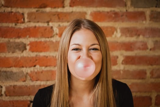 Funny girl making a pomp with a bubble gum and a brick wall of background