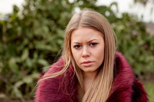 Pretty blonde girl with fur coat in the park at winter