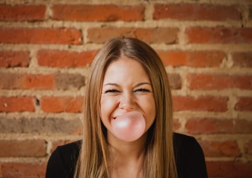 Funny girl making a pomp with a bubble gum and a brick wall of background