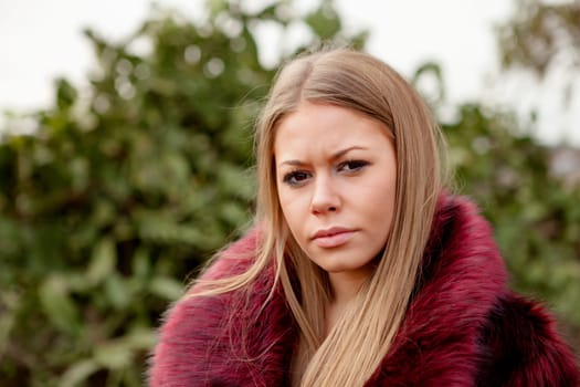 Pretty blonde girl with fur coat in the park at winter