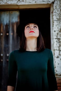 Pretty brunette girl in black with a stylish hat and a old wooden door of background