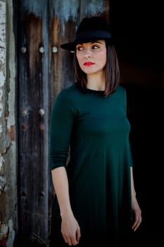 Pretty brunette girl in black with a stylish hat and a old wooden door of background