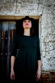 Pretty brunette girl in black with a stylish hat and a old wooden door of background