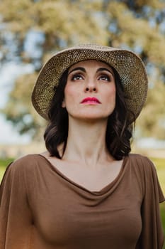 Stylish young woman with straw hat in the field looking up