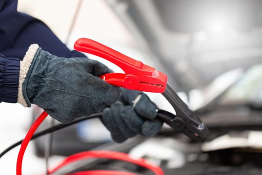 Person charging car battery with jumper cable in close up. vehicle starting close up. Hand hodling red and black power clamp in detail. Human trying repair dead motor.