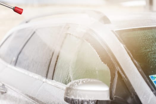 Cleaning car with water and soap in washbasin from close-up. Manual automobile washing with high pressure hose with sunlight. Touchless vehicle purifying.