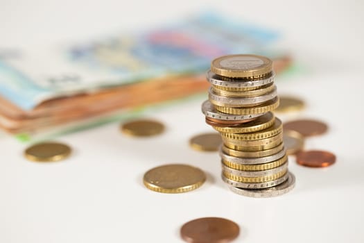 Stack of euro coins on table with paper notes in background. Metal money in a single column with cents around on white desk. Finance manegment and concept of saving salary.