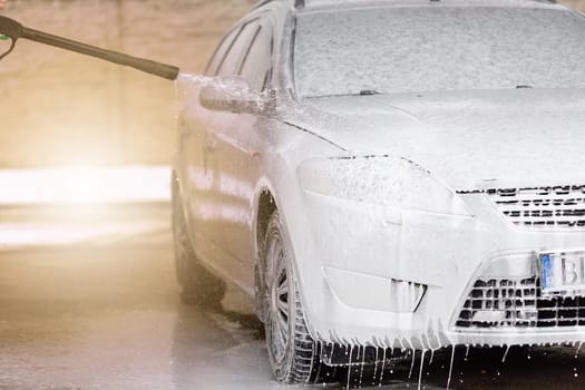 High pressure automobile cleaning with foam in carwash. Washing car by using soap and water nozzle. Vehicle purifying in self-service washbasin on sunny day.