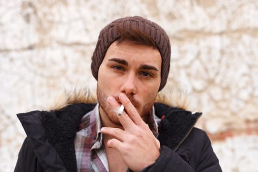 Sad guy with wool hat wearing a dark coat and smoking a cigar