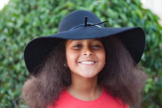 Pretty girl with long afro hair in the garden with a elegant black hat