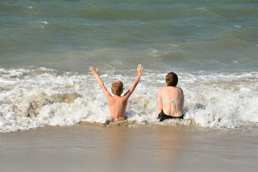 Two children sit full of joy on the sandy beach in the middle of the waves by the sea, on the North Sea coast in the Netherlands, Zeeland