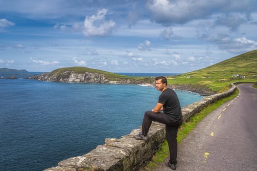 Middle age man watching and admiring amazing view of Slea Head, Coumeenoole Beach and Dingle Peninsula, part of Wild Atlantic Way, Kerry, Ireland