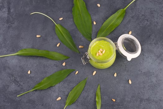 Pesto made from wild garlic, pine nuts and feta cheese in a glass, with fresh leaves on a dark textured background, empty space for text