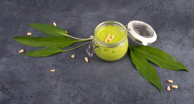 Pesto made from wild garlic, pine nuts and feta cheese in a glass, with fresh leaves on a dark textured background, empty space for text