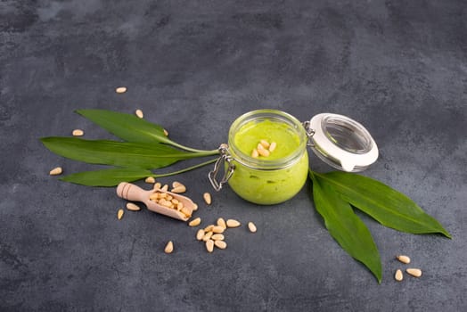 Pesto made from wild garlic, pine nuts and feta cheese in a glass, with fresh leaves on a dark textured background, empty space for text