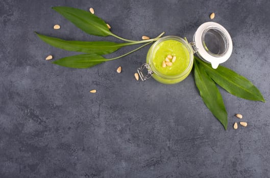 Pesto made from wild garlic, pine nuts and feta cheese in a glass, with fresh leaves on a dark textured background, empty space for text