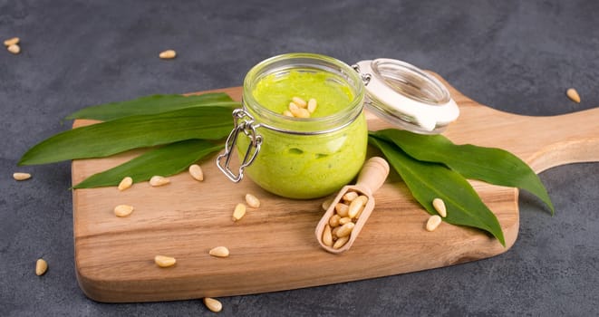 Pesto made from wild garlic, pine nuts and feta cheese in a glass, with fresh leaves on a dark textured background, empty space for text